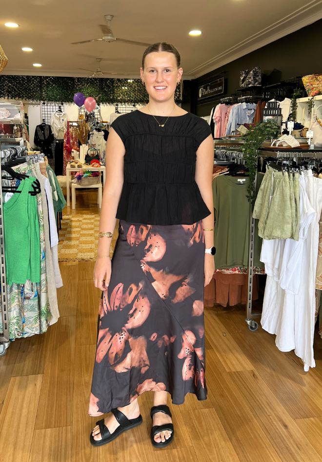Woman in a clothing store wearing a black top and floral skirt.