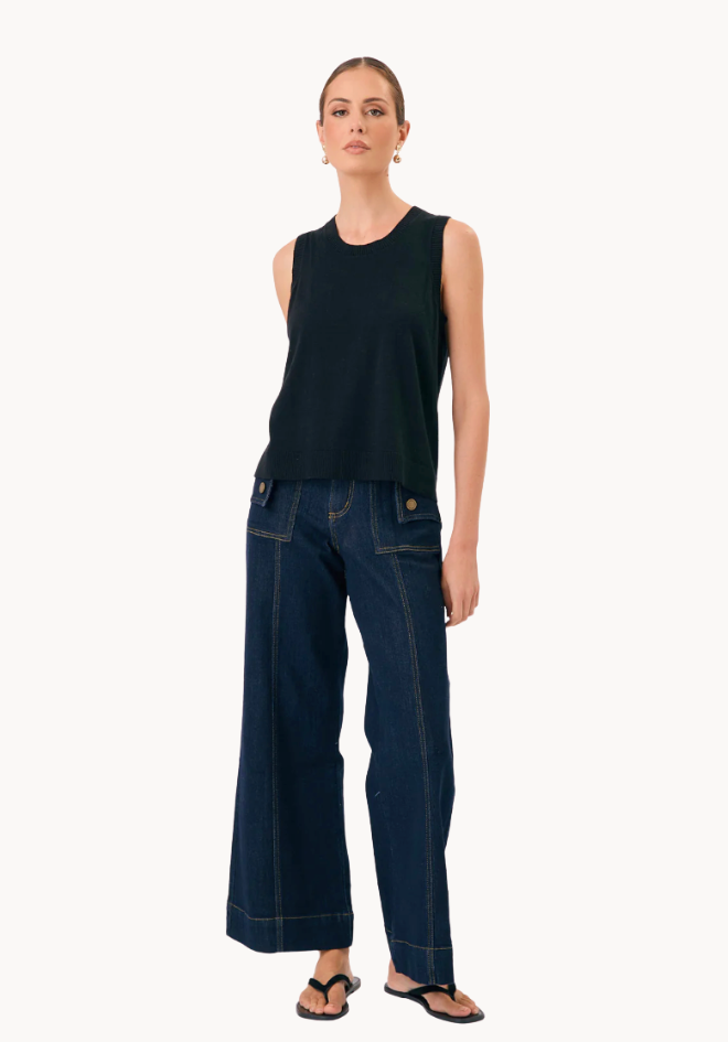 Woman wearing a black sleeveless top and dark blue jeans on a white background