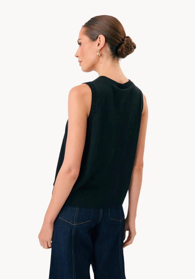 Woman wearing a black sleeveless top and dark jeans on a white background