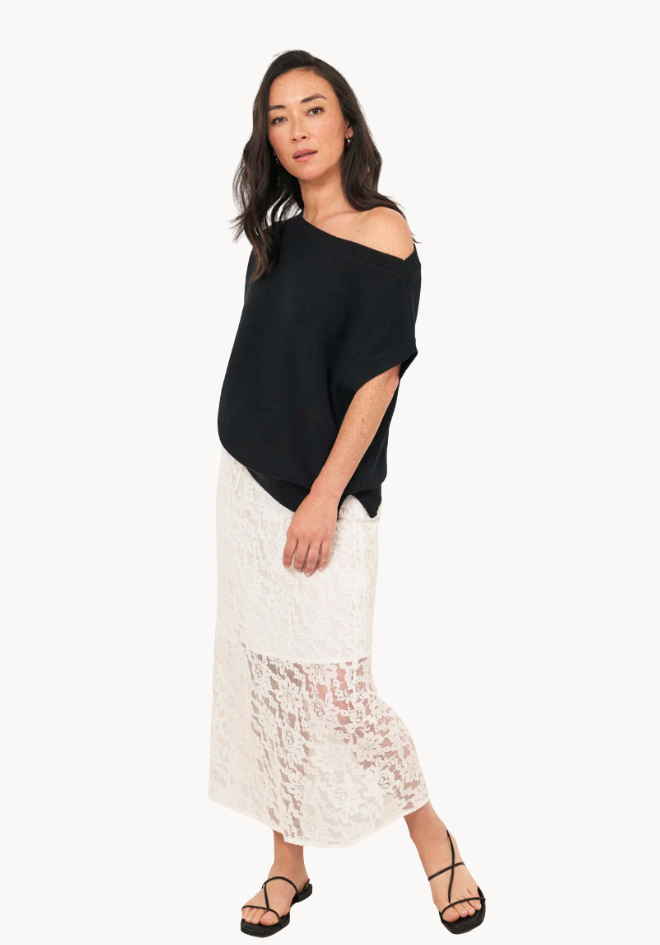 Woman wearing a black off-shoulder top and white lace skirt on a white background