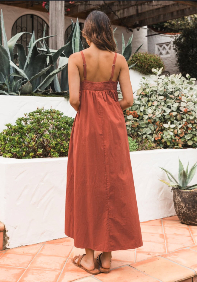 Woman in a rust-colored dress standing in a garden setting