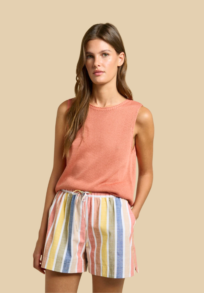 Woman wearing a sleeveless pink top and colorful striped shorts on a beige background