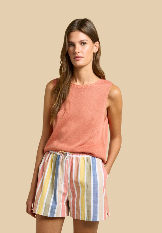 Woman wearing a sleeveless pink top and colorful striped shorts on a beige background
