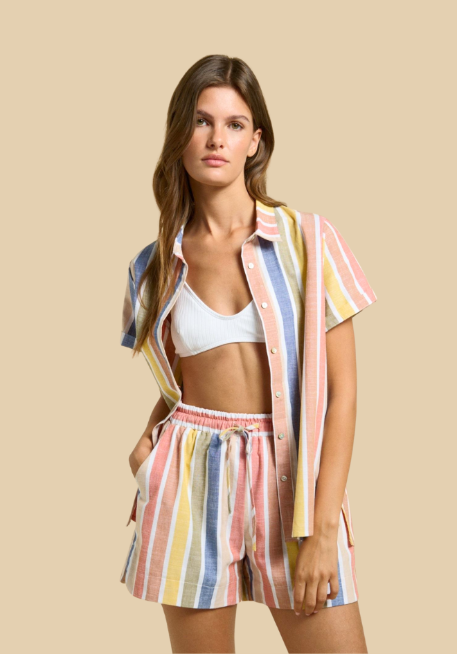 Woman wearing a colorful striped shirt and shorts set on a beige background