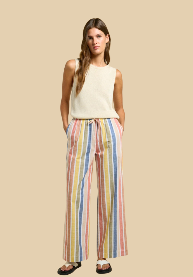 Woman wearing a sleeveless cream top and colorful striped pants on a beige background