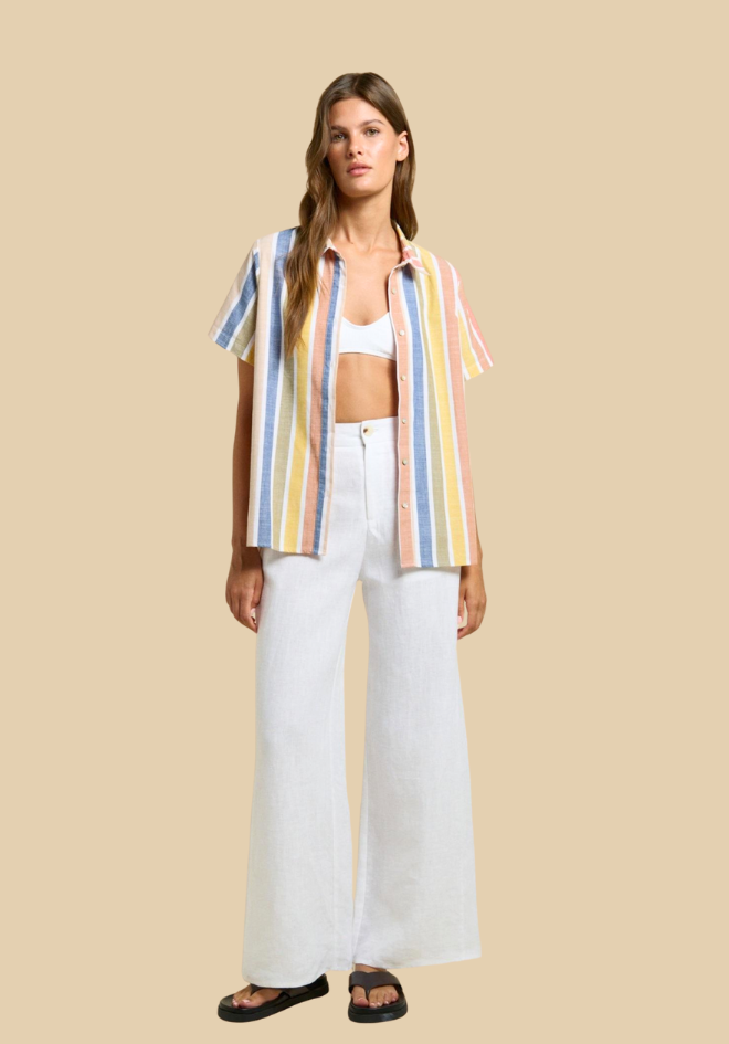 Woman wearing a colorful striped shirt and white pants on a beige background
