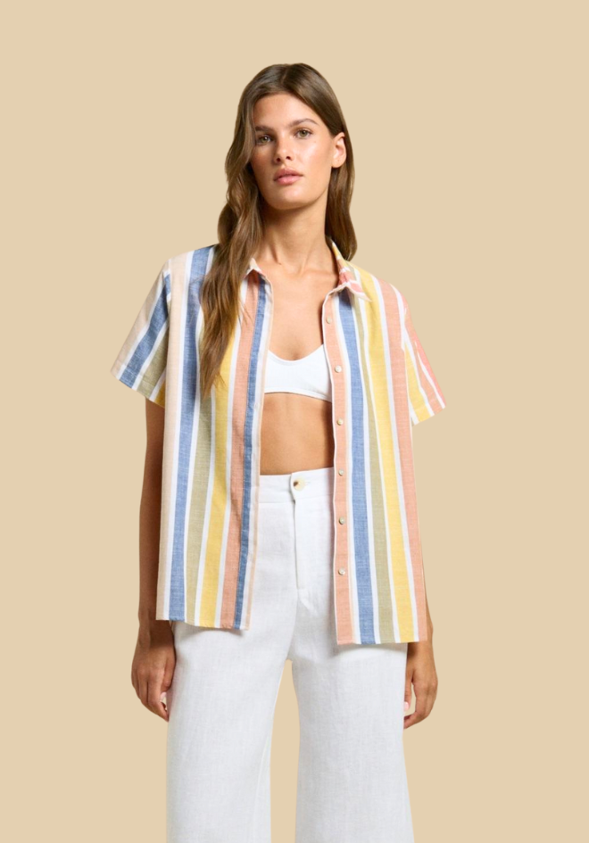 Woman wearing a colorful striped shirt over a white top and pants on a beige background