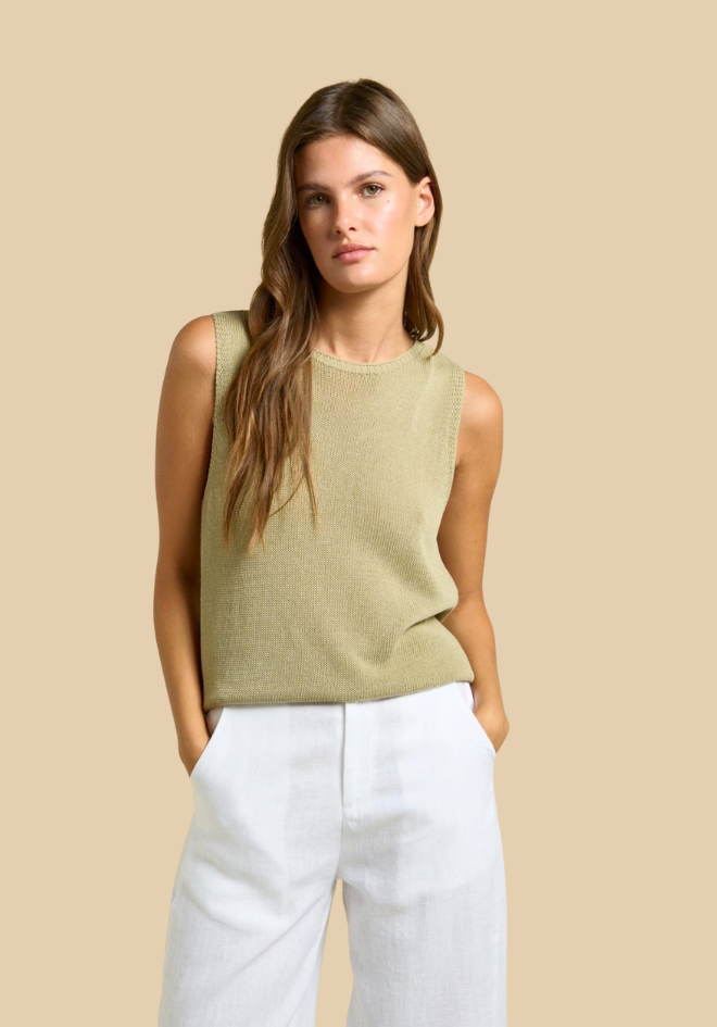 Woman wearing a green sleeveless top and white pants against a beige background