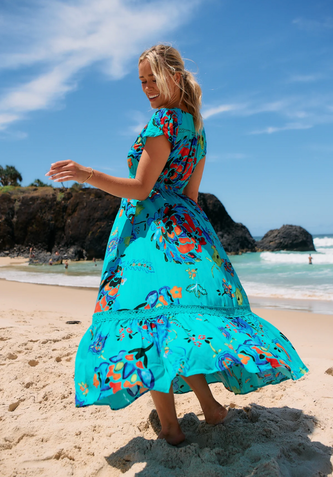 Woman in a colorful dress on a beach with blue sky and ocean.
