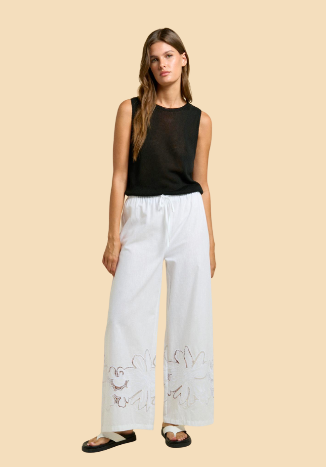 Woman wearing a black sleeveless top and light blue pants with embroidery on a beige background