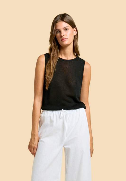 Woman wearing a black sleeveless top and white pants against a beige background