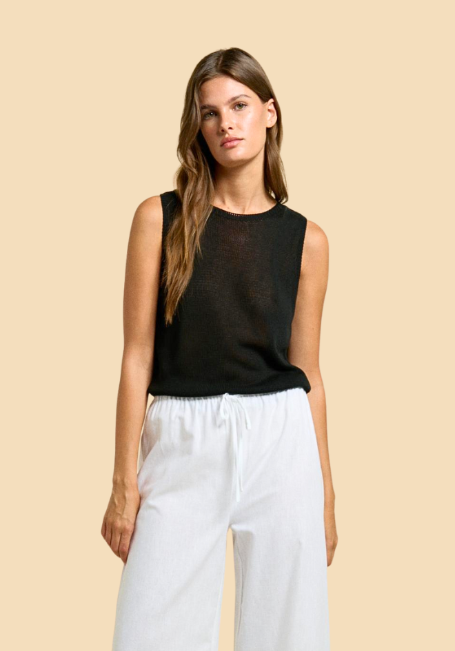 Woman wearing a black sleeveless top and white pants against a beige background