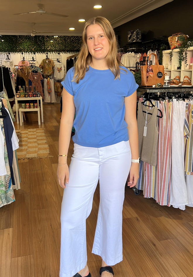 Woman in a blue shirt and white pants standing in a clothing store.