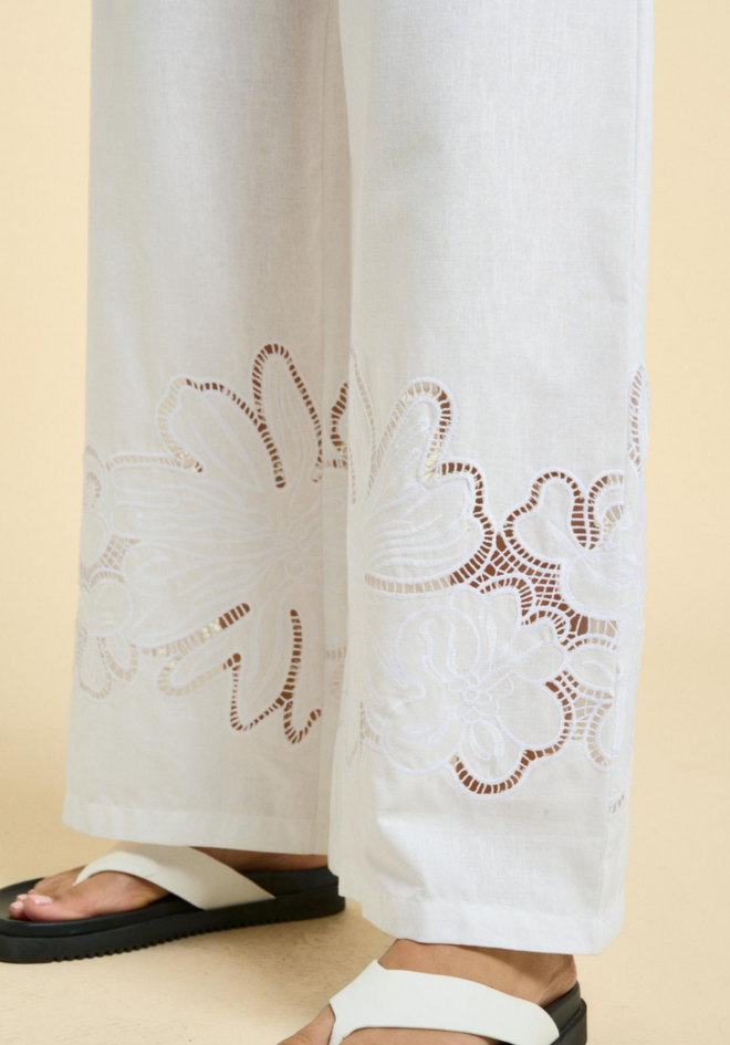White pants with intricate brown embroidery on a beige background