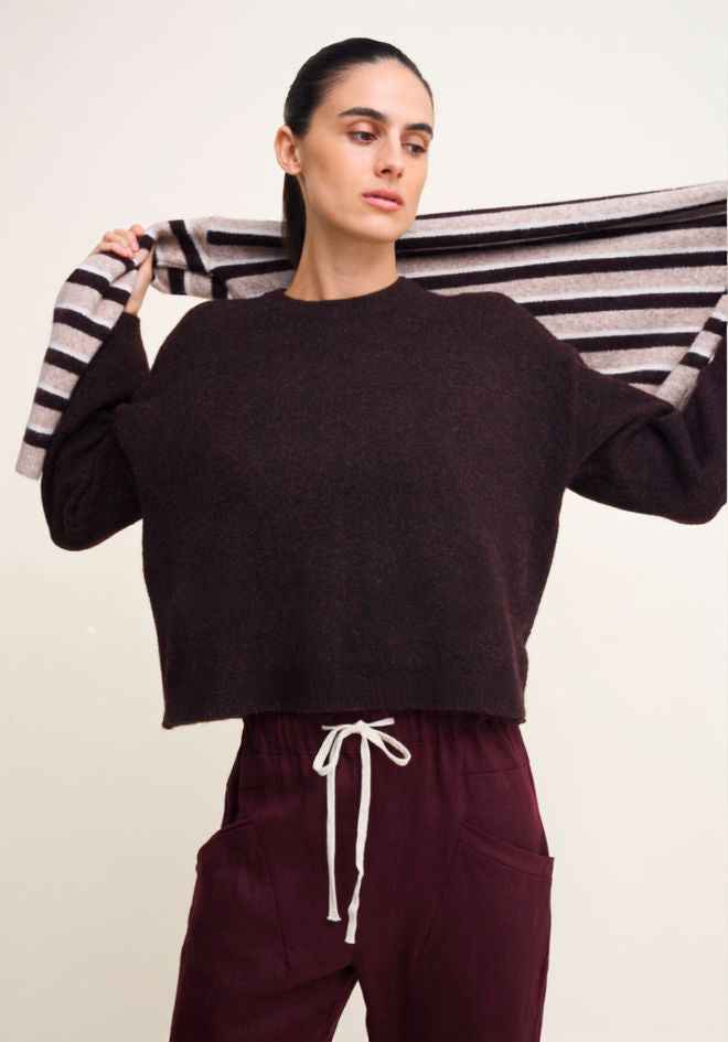Little Lies Otto Knit in Rich Chocolate — editorial shot of cropped chocolate wool blend knit with drawstring hem, model holding Otto Knit stripe version overhead, styled with deep plum drawstring pants, available in Australia at Kat and Ko Clothing