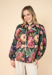 Estelle Print Blouse by Fria The Label — front view of floaty dark floral blouse with bold peony print, ruffled neckline and balloon sleeves, styled with white pants, available in Australia at Kat and Ko Clothing