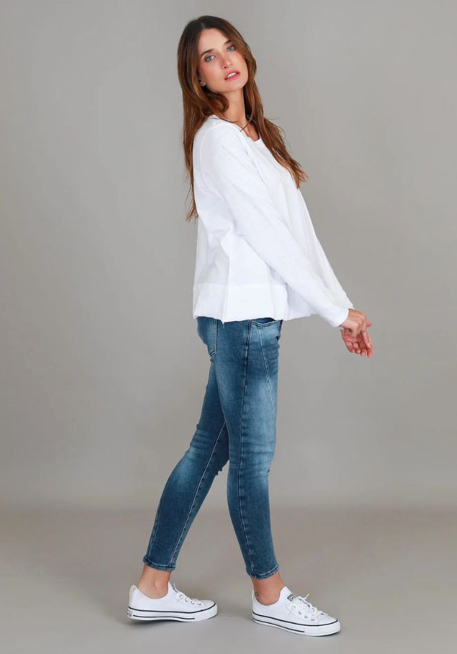 3rd Story The Label Sonya L/S Tee White — side walking view of relaxed white long sleeve tee with curved hem, styled with blue skinny jeans and white Converse sneakers, available in Australia at Kat and Ko Clothing