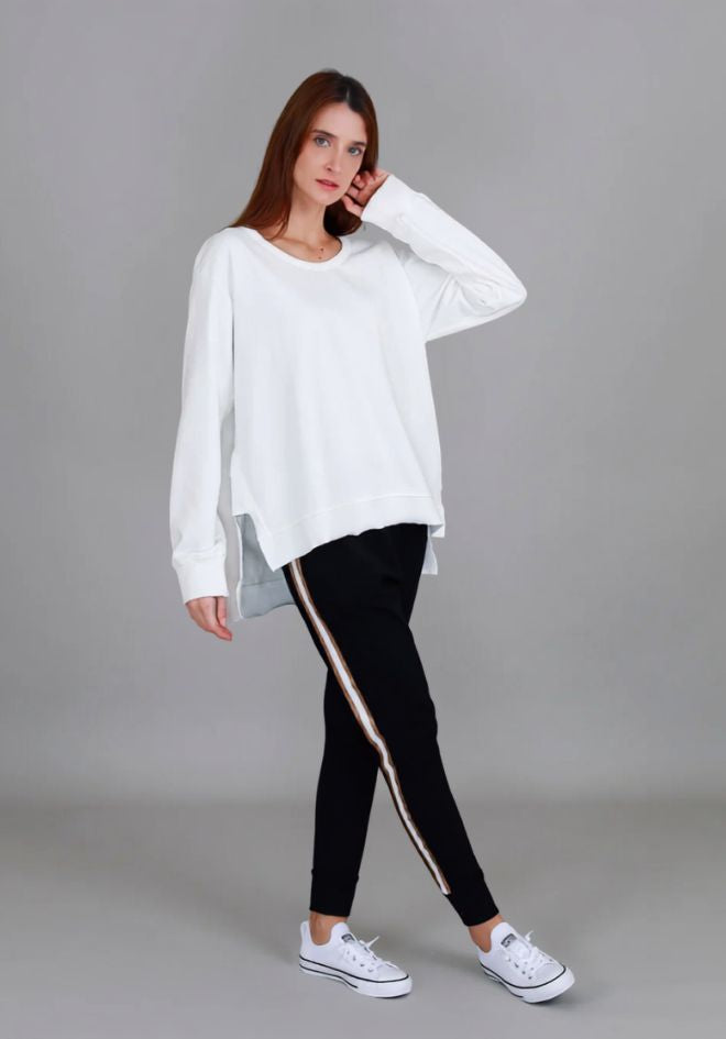 Ulverstone Sweater in White by 3rd Story The Label — angled front view of oversized white long sleeve scoop neck sweater with high-low hem, styled with black side-stripe jogger pants and white Converse sneakers, available in Australia at Kat and Ko Clothing