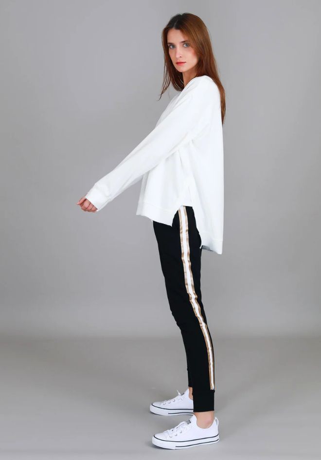 3rd Story The Label Ulverstone Sweater White — side view of oversized white long sleeve sweater with curved high-low hem and side splits, styled with black gold-stripe jogger pants and white Converse sneakers, available in Australia at Kat and Ko Clothing