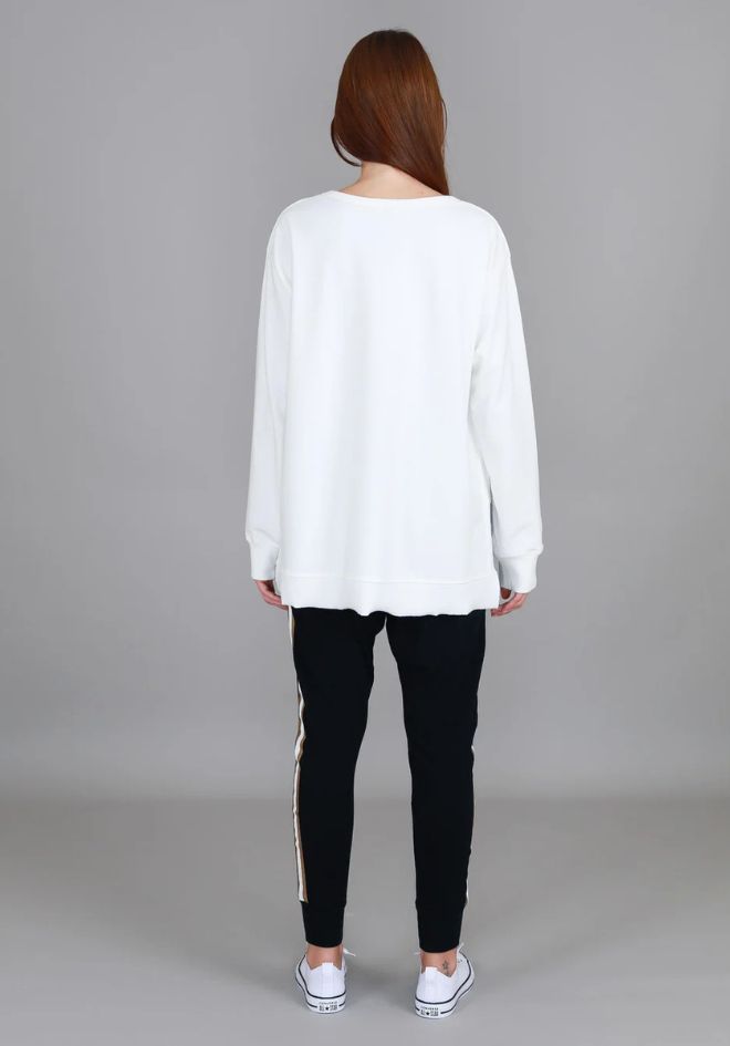 3rd Story The Label Ulverstone Sweater White — back view of oversized white long sleeve sweater with curved high-low hem and side splits, styled with black gold-stripe jogger pants and white sneakers, available in Australia at Kat and Ko Clothing