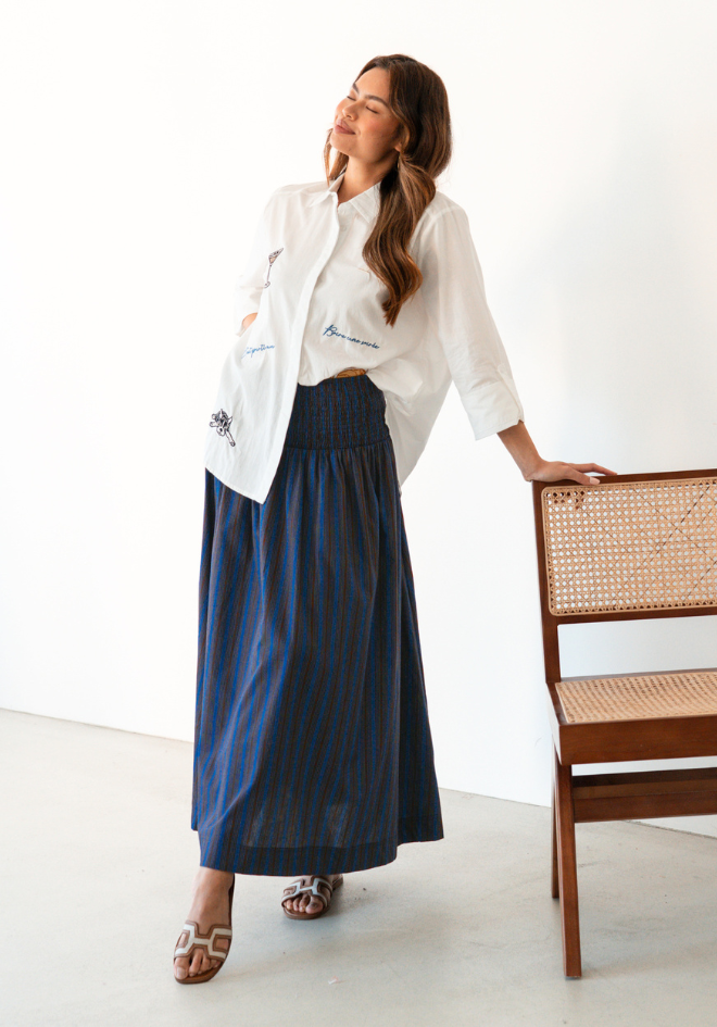 Charli Skirt Label of Love — lifestyle shot of chocolate and cobalt blue stripe cotton maxi skirt styled with a white linen shirt and heeled sandals, available in Australia at Kat and Ko Clothing