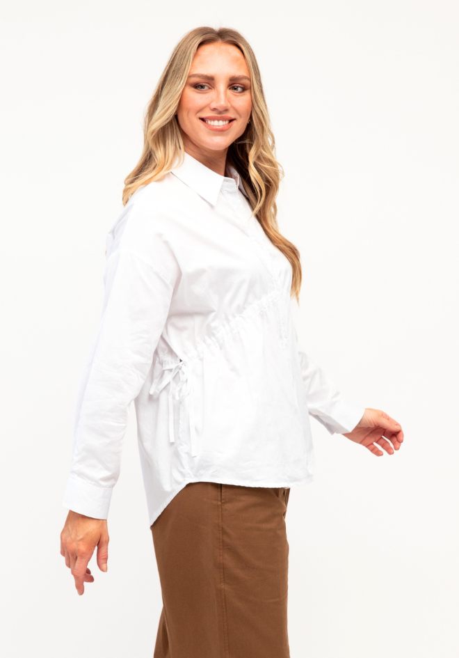 Kori Shirt Label of Love — side view of white cotton shirt highlighting the side tie waist detail and curved hem, styled with tan trousers, available in Australia at Kat and Ko Clothing